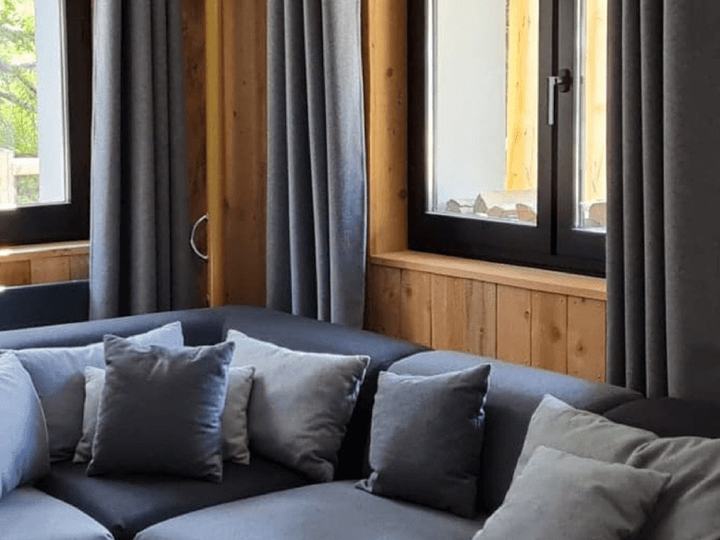 Canapé d’angle gris et coussins dans le salon d’un chalet, avec rideaux gris et boiseries