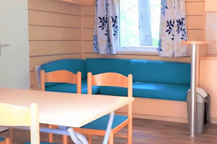 Intérieur de mobil-home avec banquette bleue en simili-cuir rénovée et rideaux imprimés