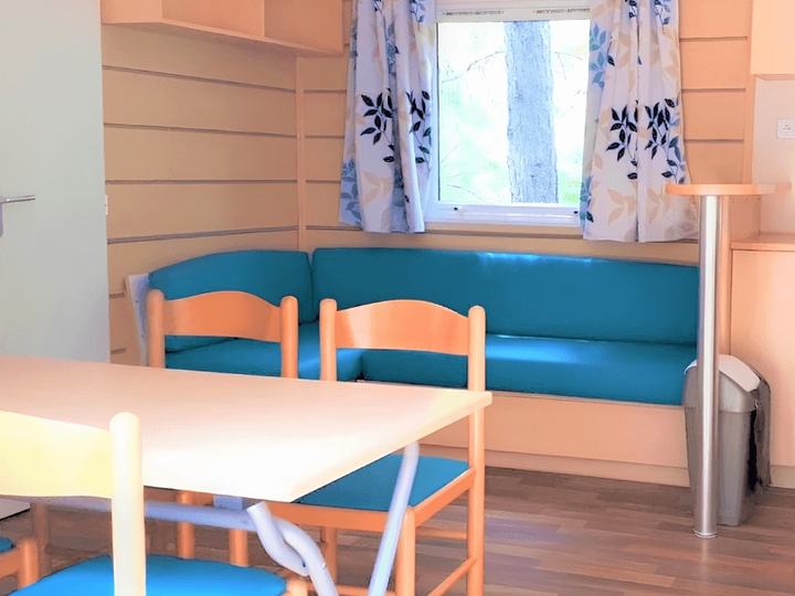 Intérieur de mobil-home avec banquette bleue en simili-cuir rénovée et rideaux imprimés