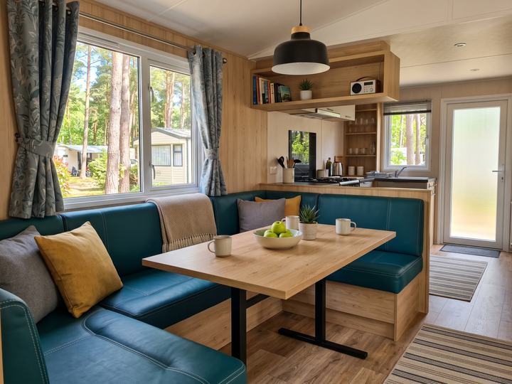 Intérieur de mobil-home rénové : banquette en simili-cuir vert-bleu, table en bois clair et rideaux imprimés