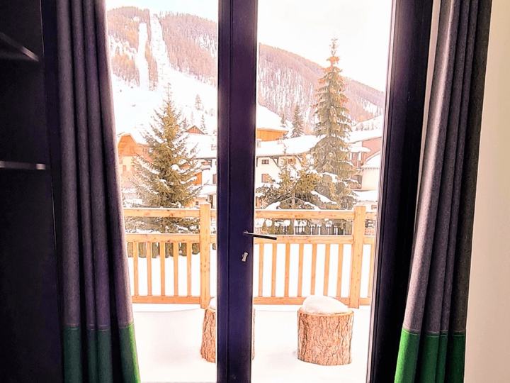 Rideaux gris et verts confectionnés sur mesure devant une porte-fenêtre avec vue sur la neige