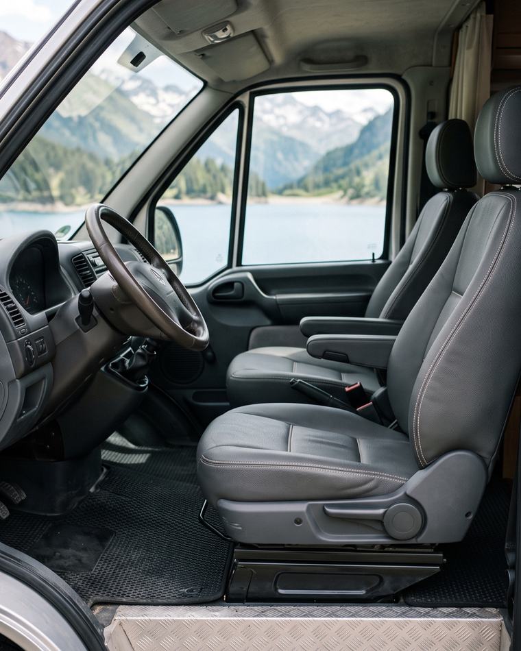 Sièges de cabine de camping-car recouverts de simili-cuir gris, vue sur un lac de montagne