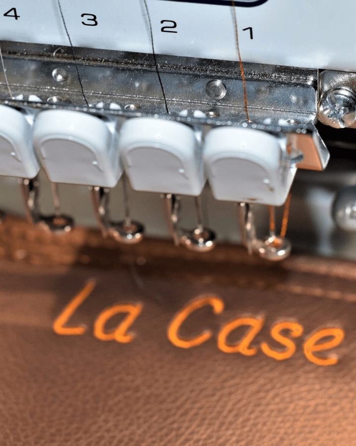 Tête de la brodeuse professionnelle de l’atelier brodant un texte orange sur du simili-cuir marron